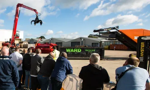 Group of onlookers watch a crane in a scrap yard